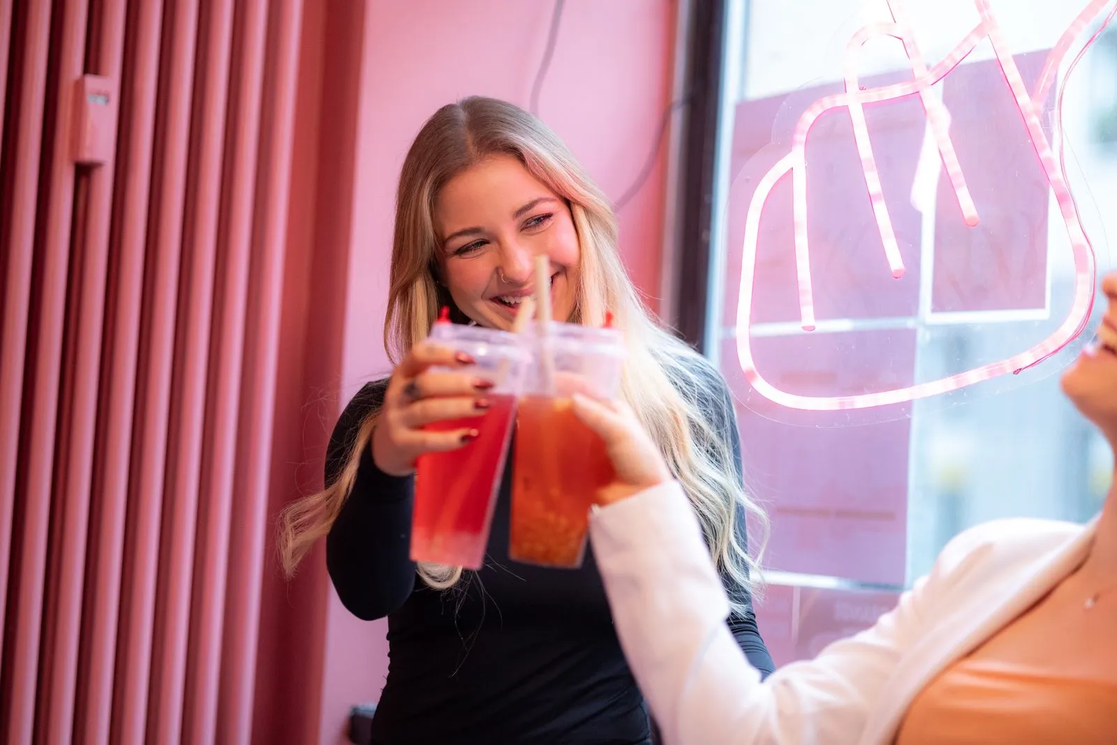 Two women smiling while toasting bubble tea in a vibrant indoor setting.